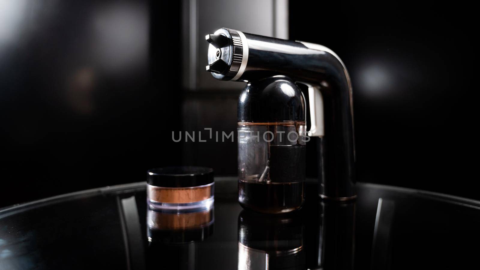 A close-up of the instant tanning equipment. Gun spraying paint for leather and matting body powder on a black background.