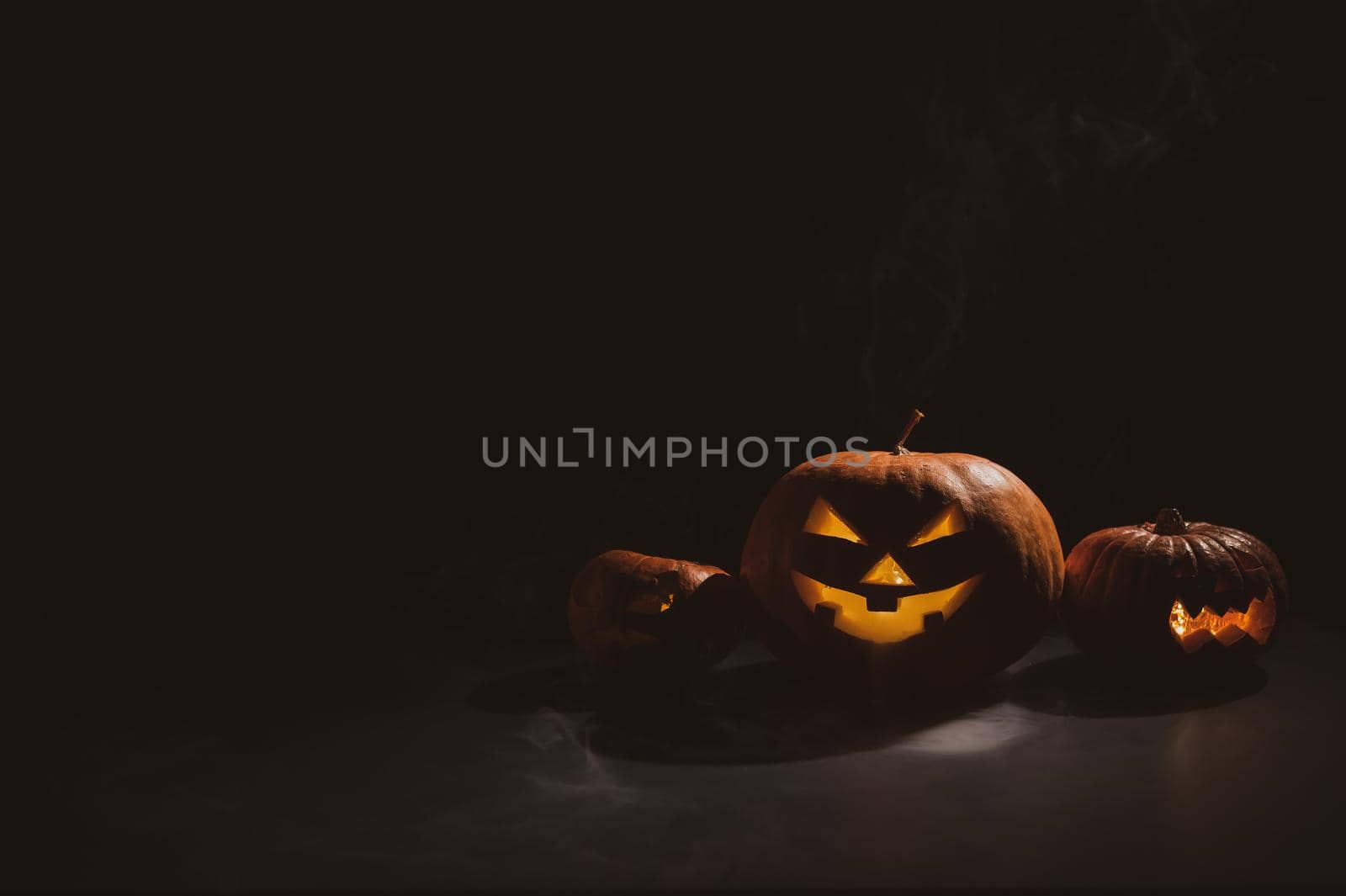 Pumpkins with carved grimaces and candles inside in the dark for halloween. Jack o latern in smoke. by mrwed54