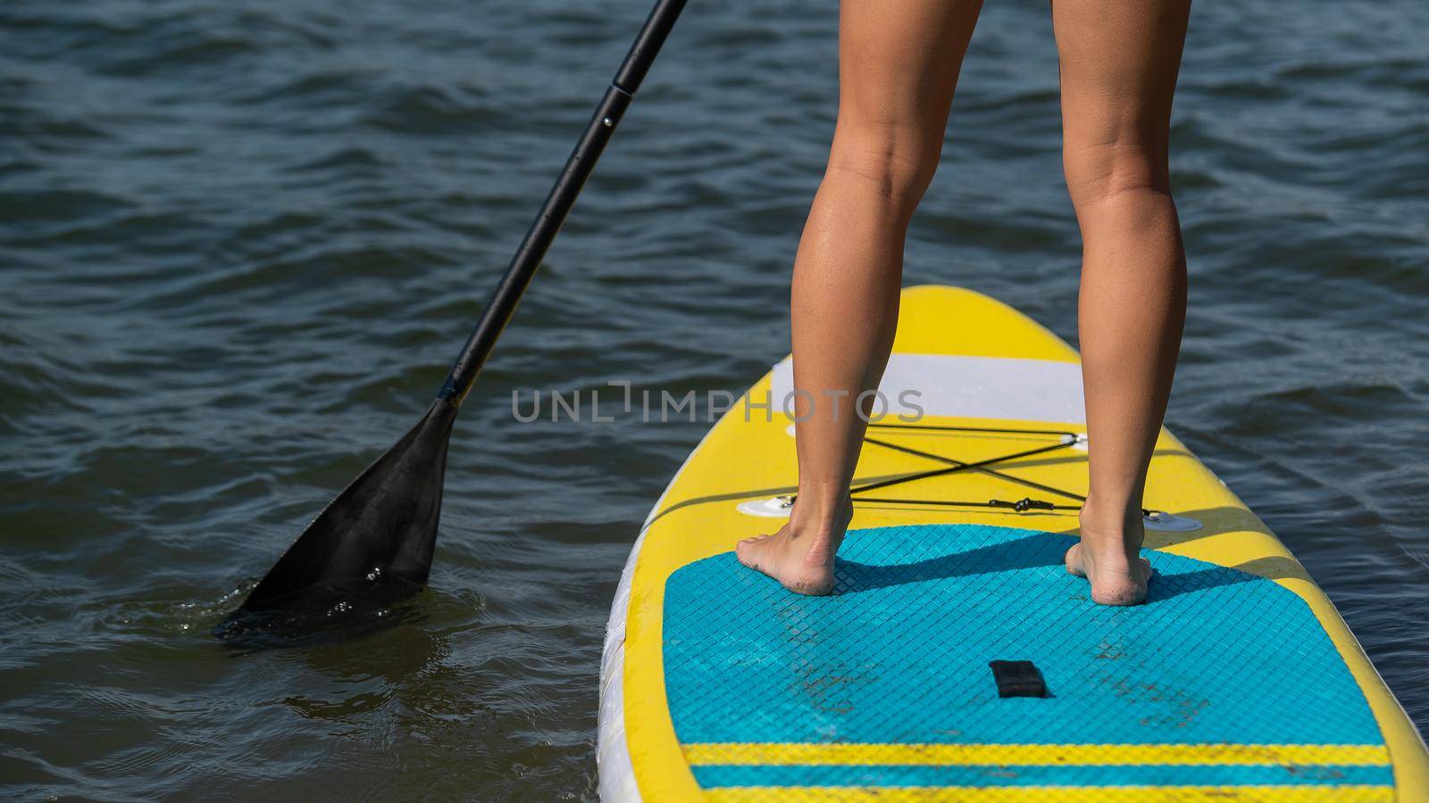 Caucasian woman swims on a SUP board. Close-up of female legs on the surf. by mrwed54