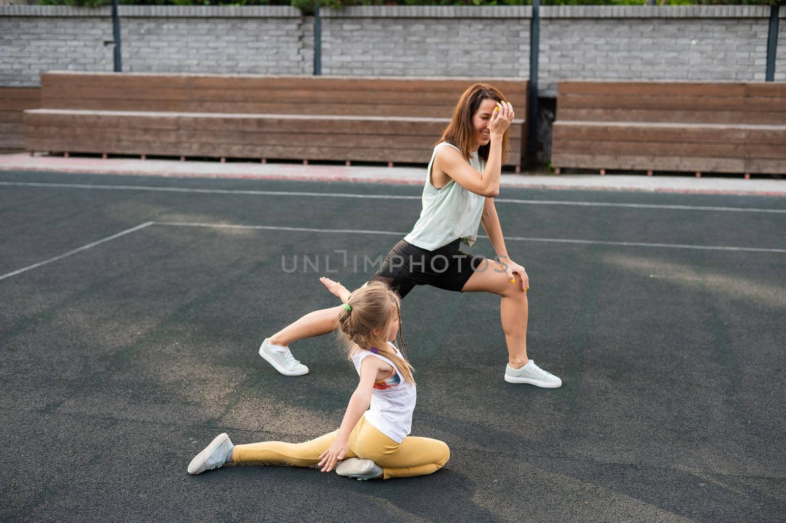 Caucasian woman goes in for sports with her daughter outdoors. A schoolgirl and her mother are running around in the stadium