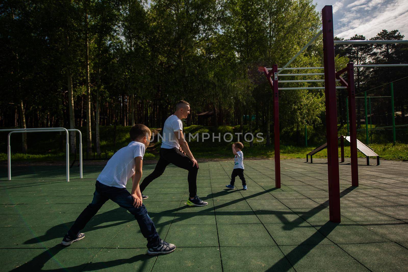 Caucasian man and two boys doing exercises outdoors. Father and sons train on the sports ground.