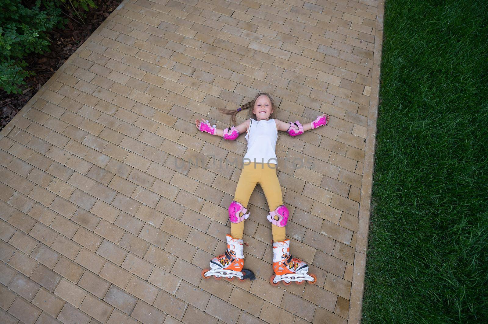 Little girl learns to roller skate and falls. View from above.