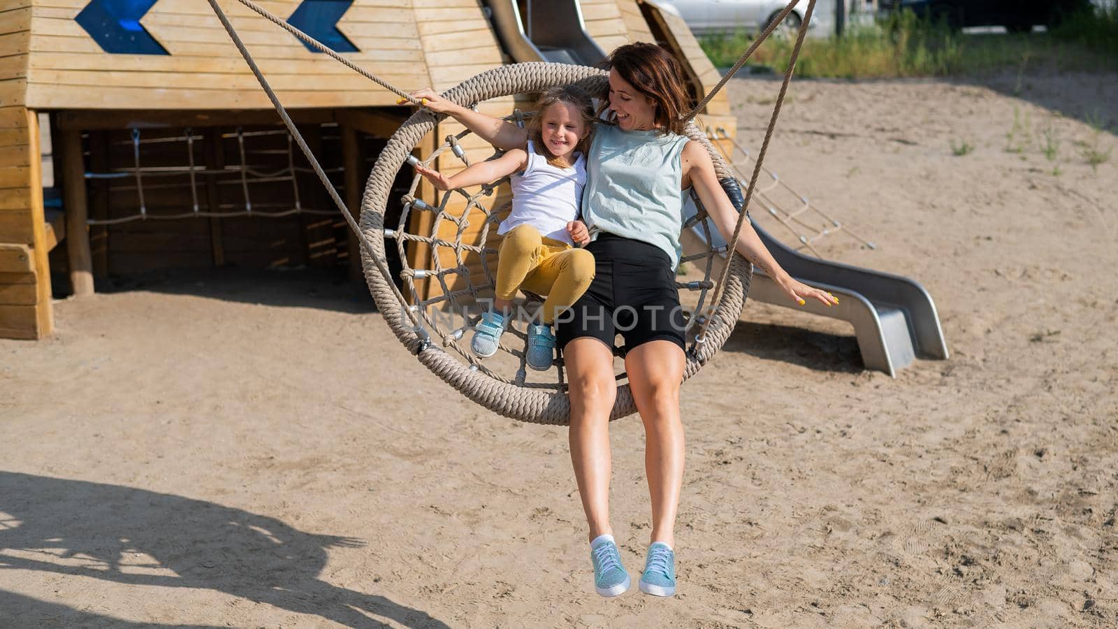 Mom and daughter swing on a round swing. Caucasian woman and little girl have fun on the playground