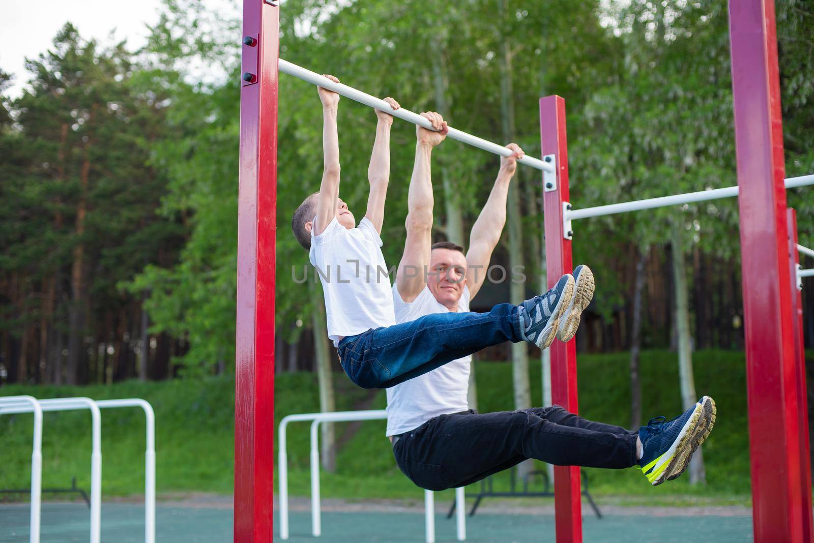 Caucasian man trains a boy on the horizontal bar on the playground. Dad and son go in for outdoor sports. by mrwed54