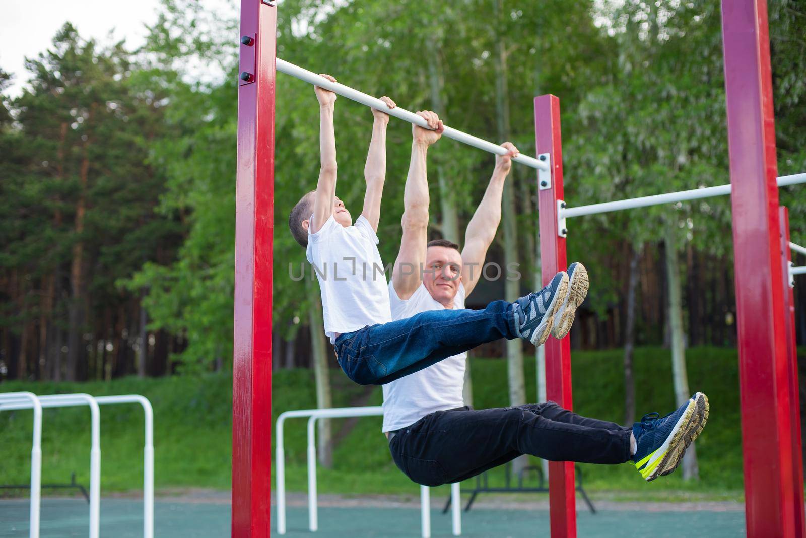 Caucasian man trains a boy on the horizontal bar on the playground. Dad and son go in for outdoor sports