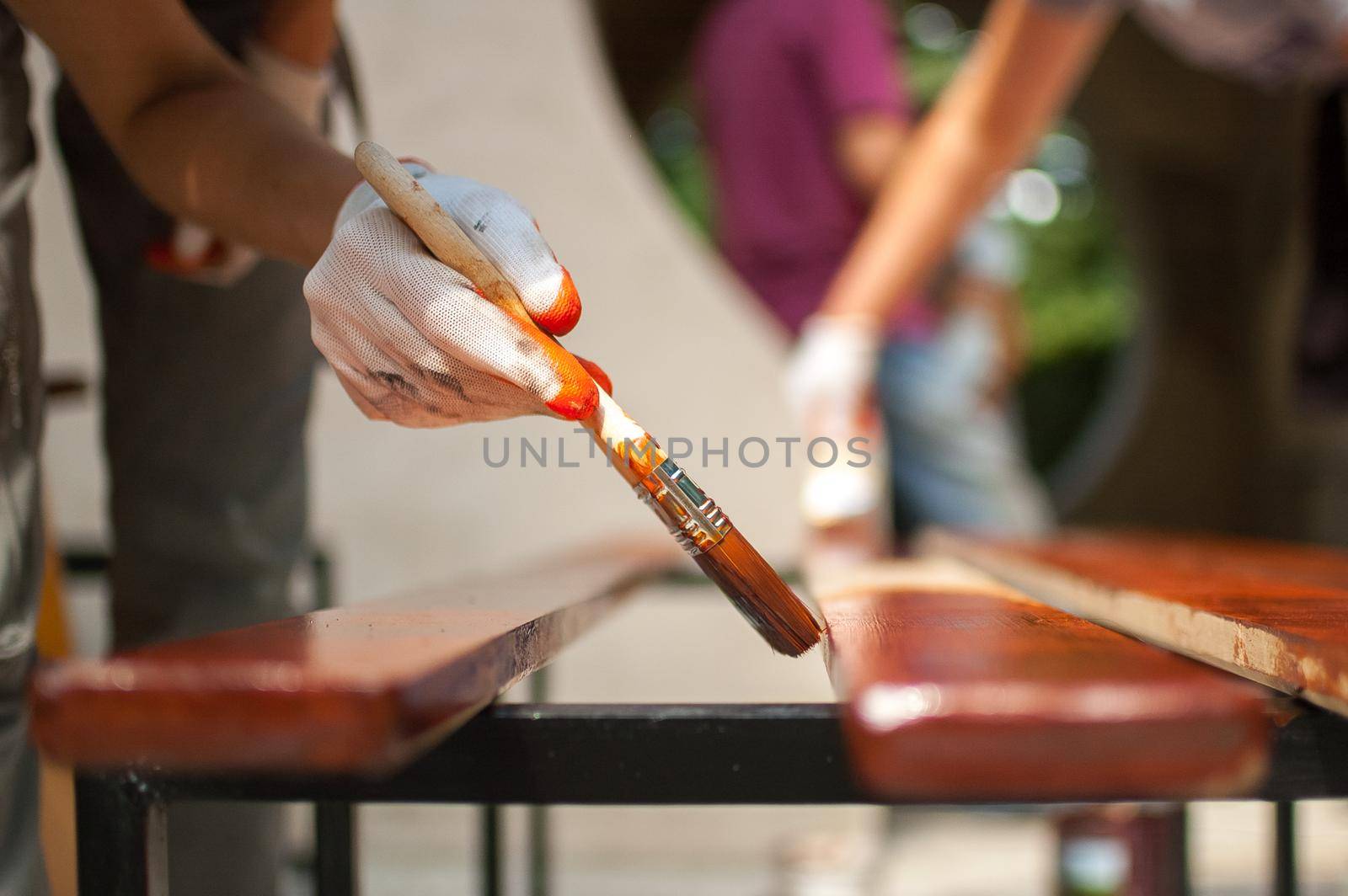 Female worker makes painting works of wooden products, plank with brown paint for making bench, carpenters work, wood covering protection. by balinska_lv