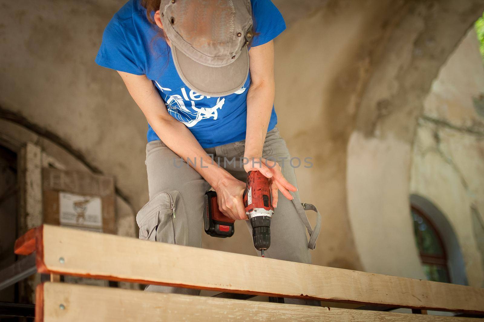 Skilled young female worker is using power screwdriver drilling during construction wooden bench gender equality, feminism, do it yourself concepts. by balinska_lv