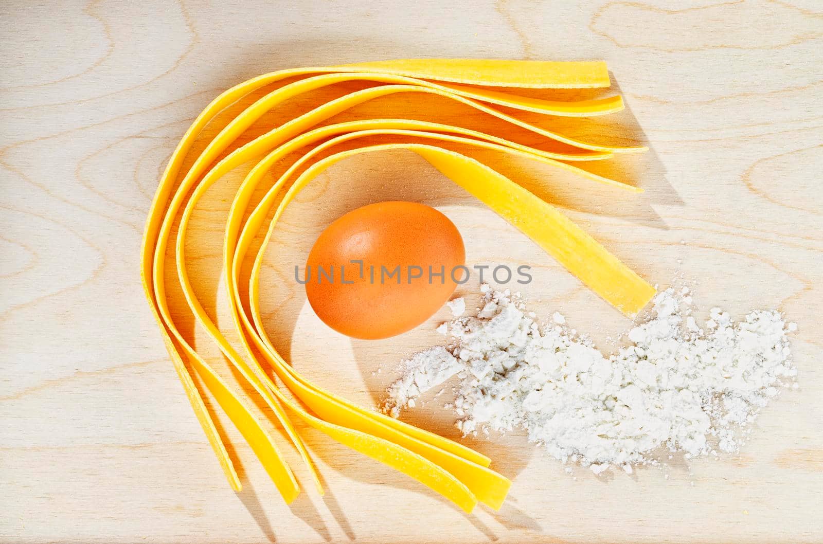 Large flat egg  pasta pappardelle on wooden background with egg and flour