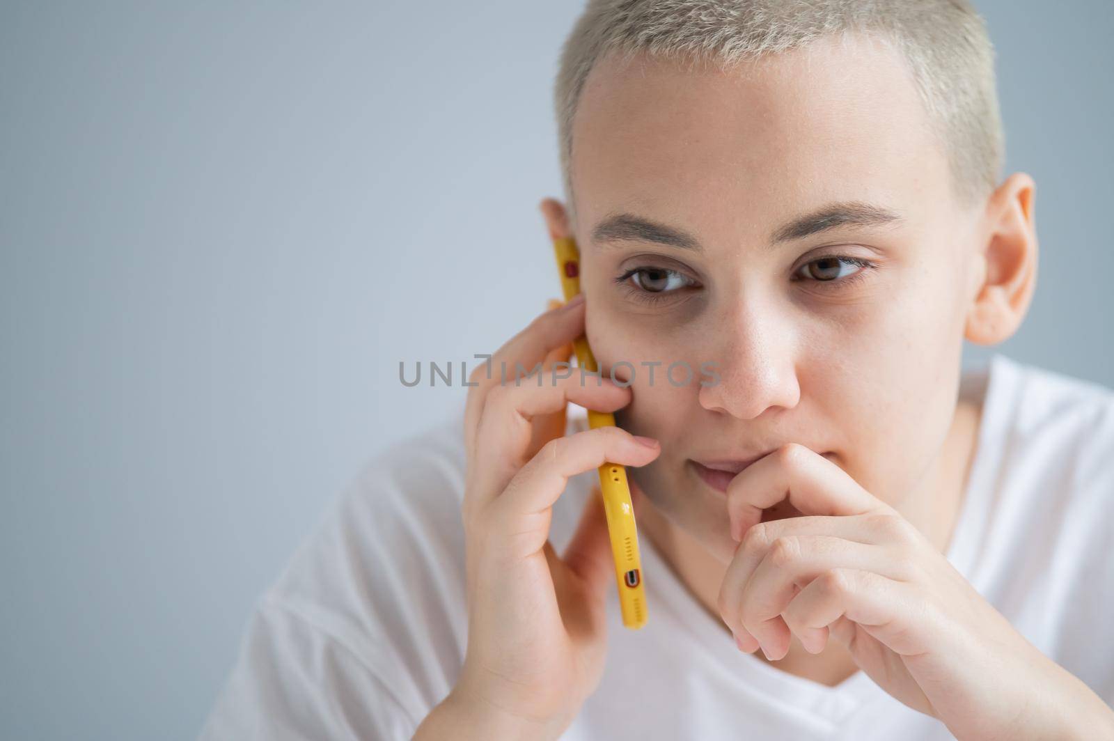 A pensive young woman with a short haircut talks thoughtfully on a mobile phone on a white background.