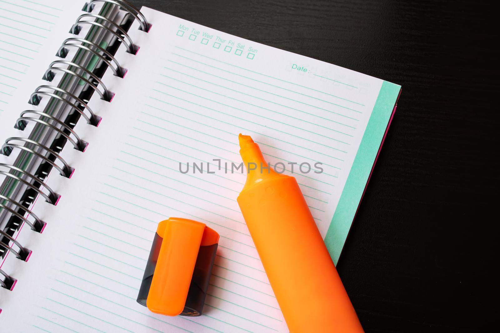 Orange marker and notebook on a black wooden table