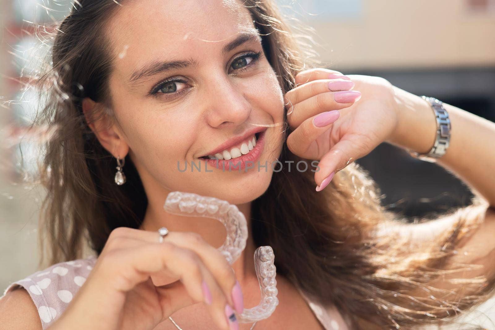 Beautiful caucasian woman holding transparent mouth guards for bite correction. Girl with silicone braces outdoors. by mrwed54