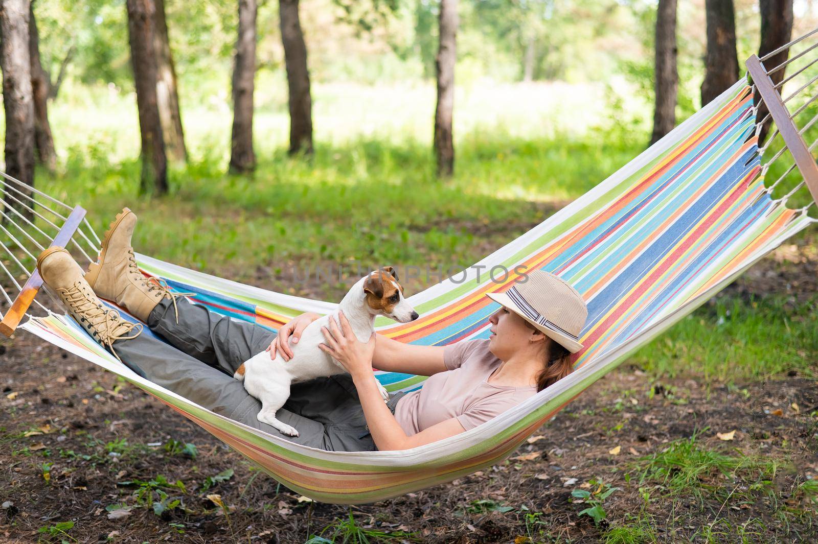 Caucasian woman lies in a hammock with Jack Russell Terrier dog in a pine forest by mrwed54