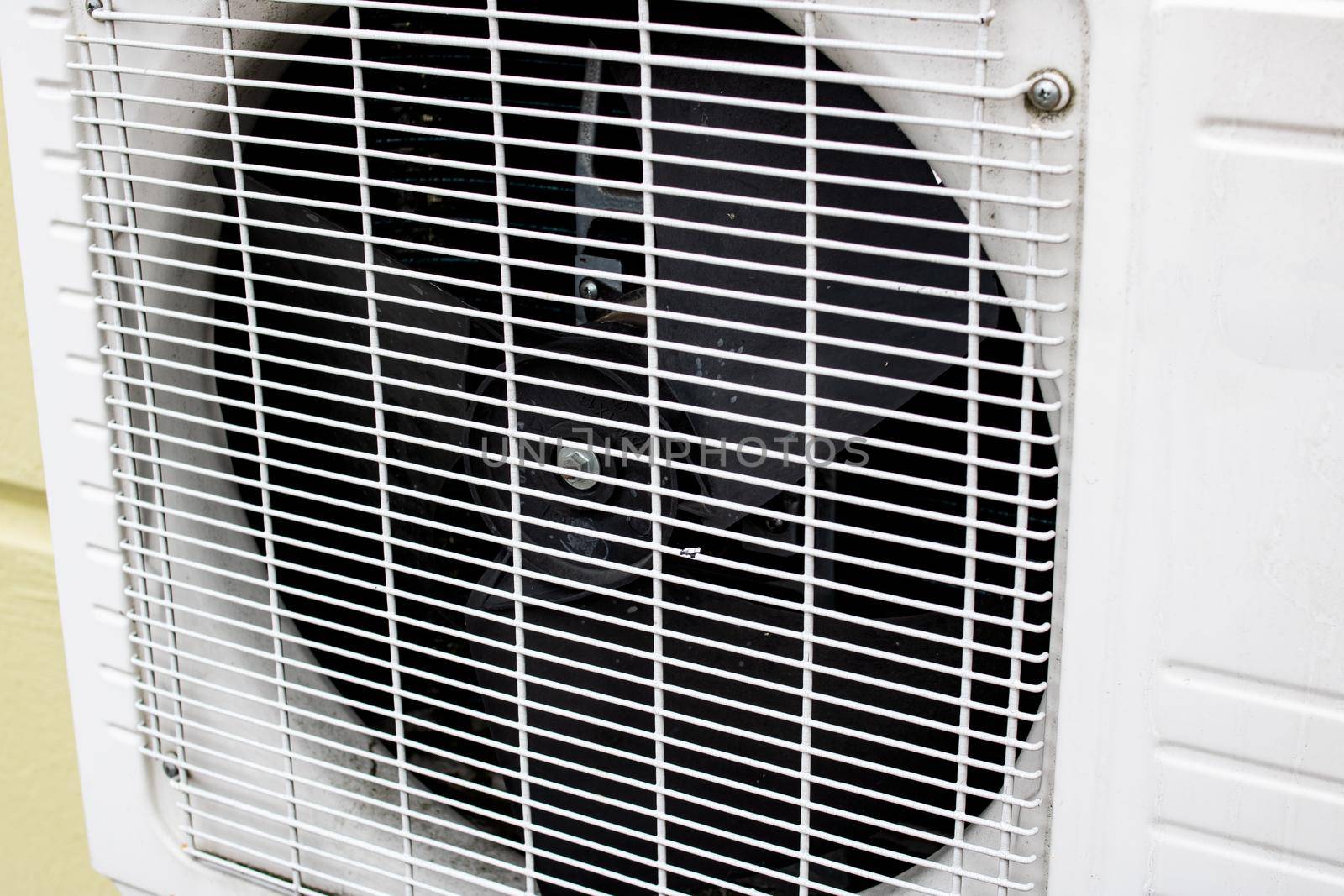 Gray air conditioner fan behind bars close up