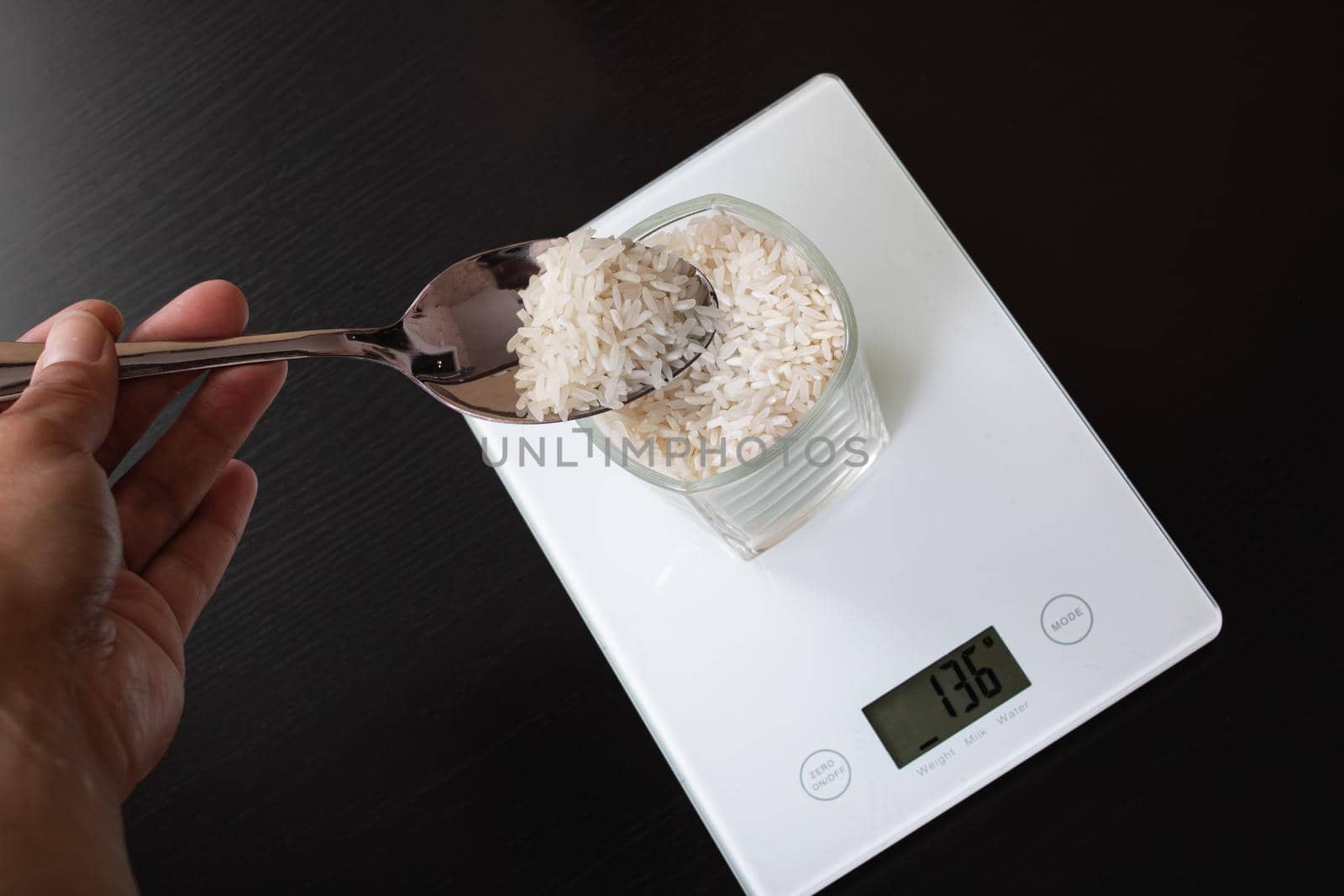 Glass with rice on electronic scales and spoon close up