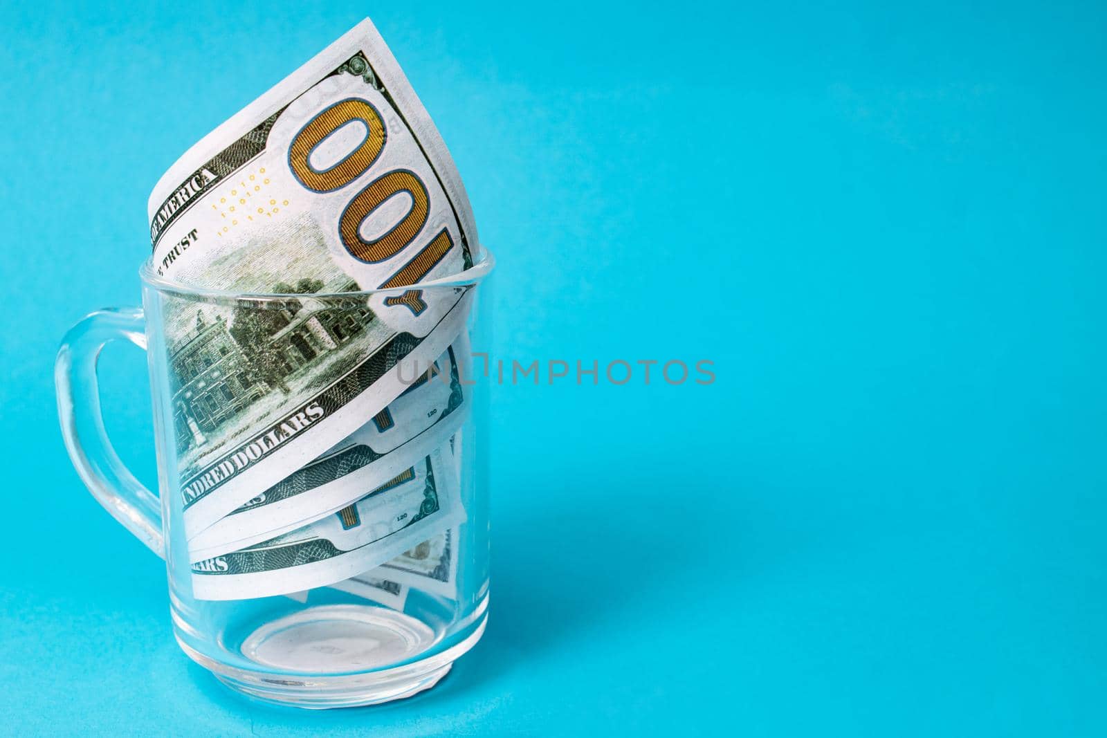 Dollar bills in a transparent mug on a blue background, copy space