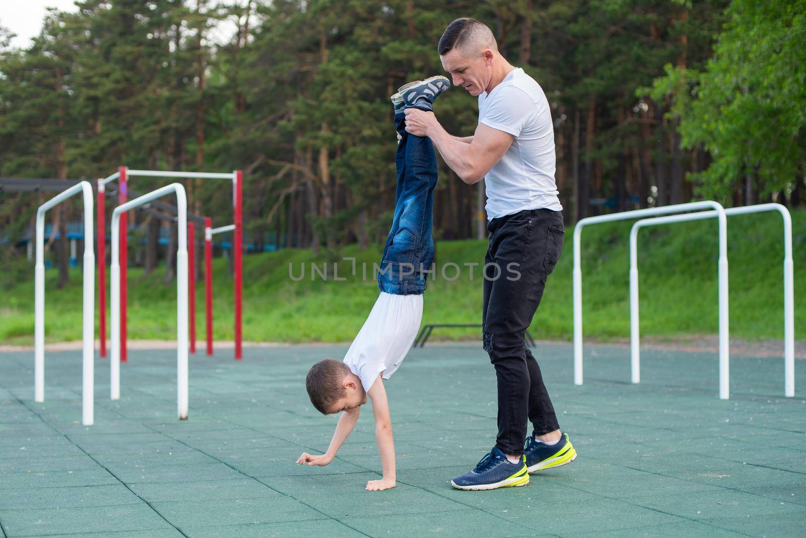 Caucasian man teaching son handstand at playground. by mrwed54