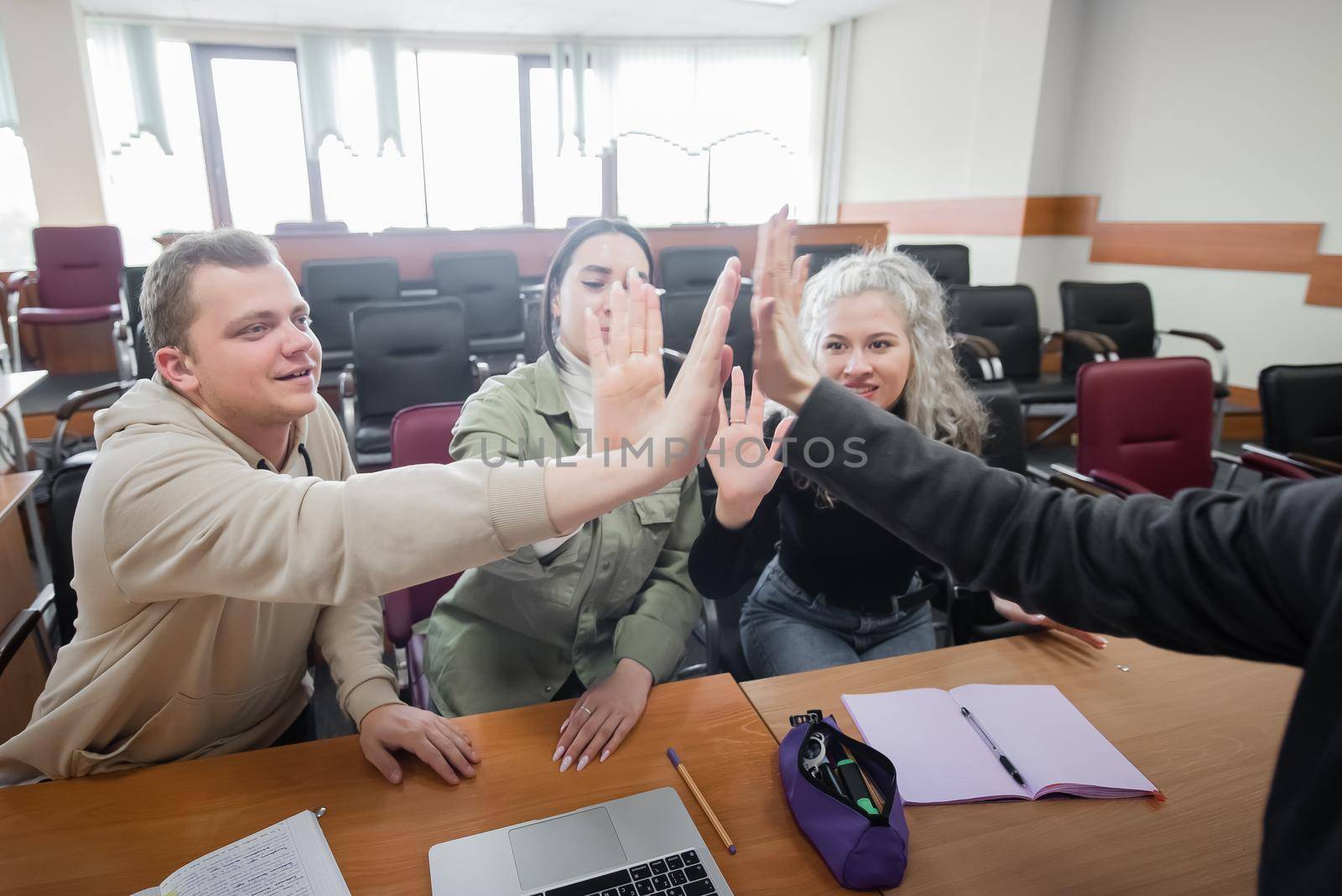 Students and lecturer give a high five in the university classroom. by mrwed54