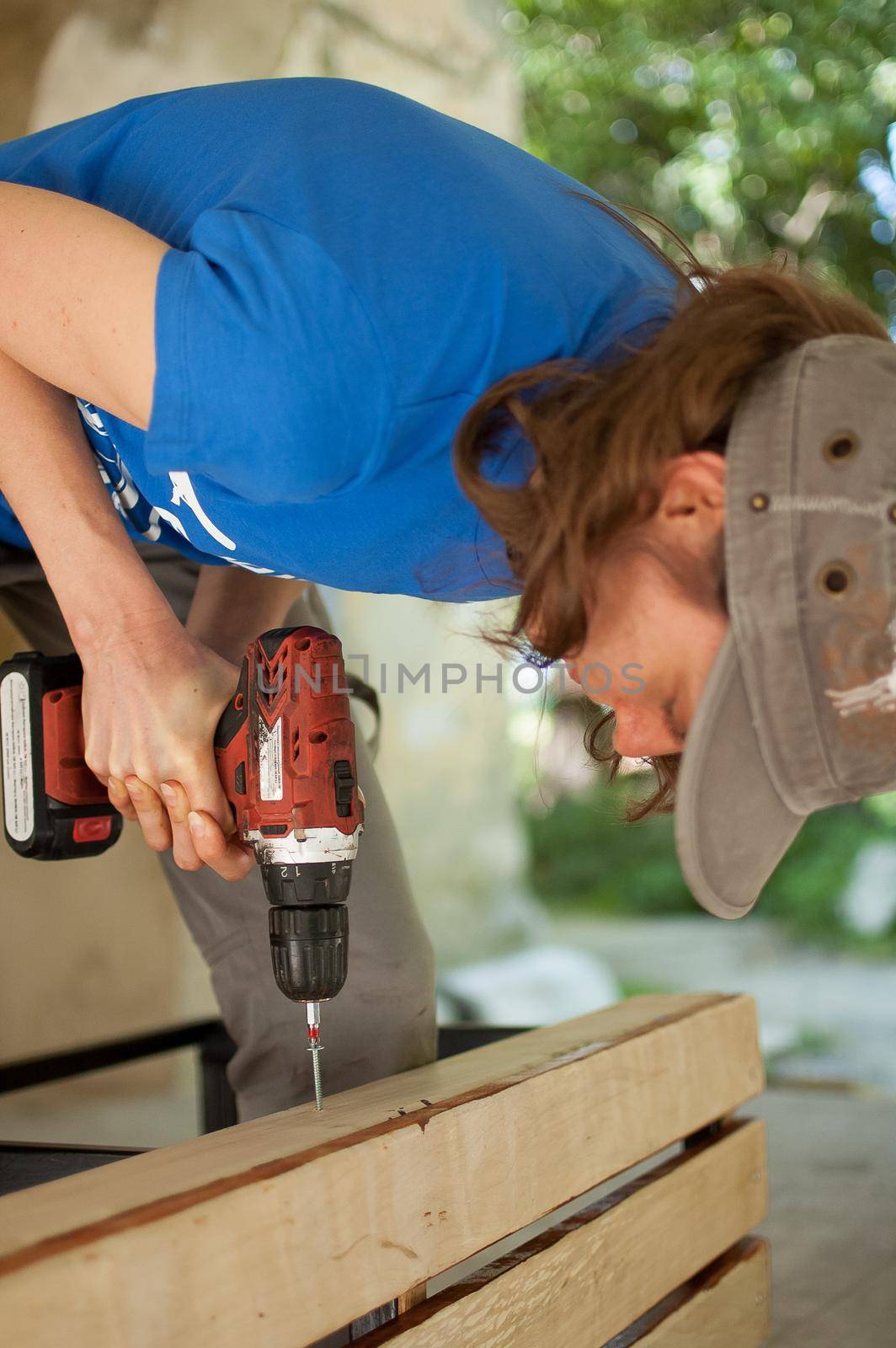 Skilled young female worker is using power screwdriver drilling during construction wooden bench gender equality, feminism, do it yourself concepts. by balinska_lv