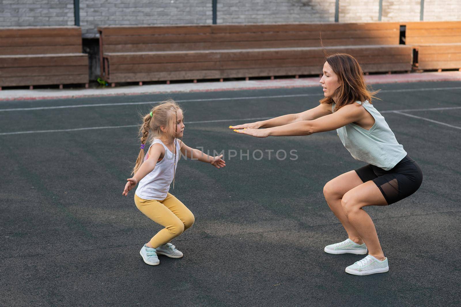 Mother and daughter go in for sports outdoors. Caucasian woman and little girl are engaged in fitness at the stadium. by mrwed54