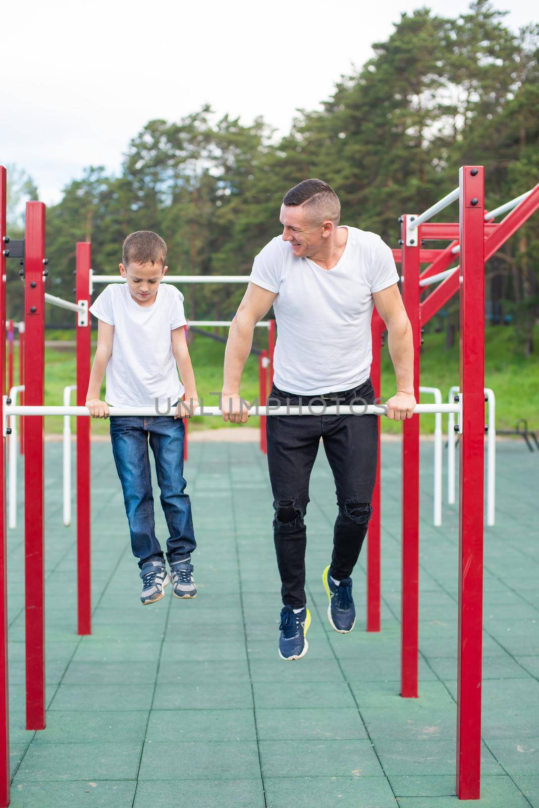 Caucasian man trains a boy on the uneven bars on the playground. Dad and son go in for outdoor sports. by mrwed54