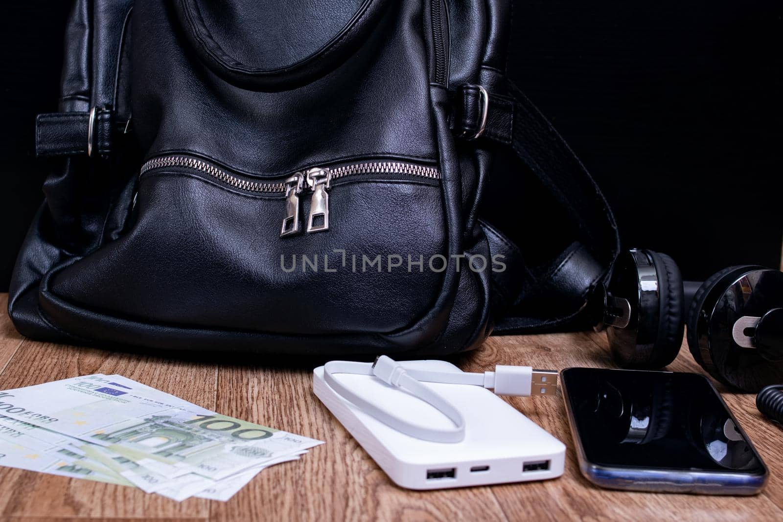 Mobile phone, power bank, bag, money and headphones on a wooden table