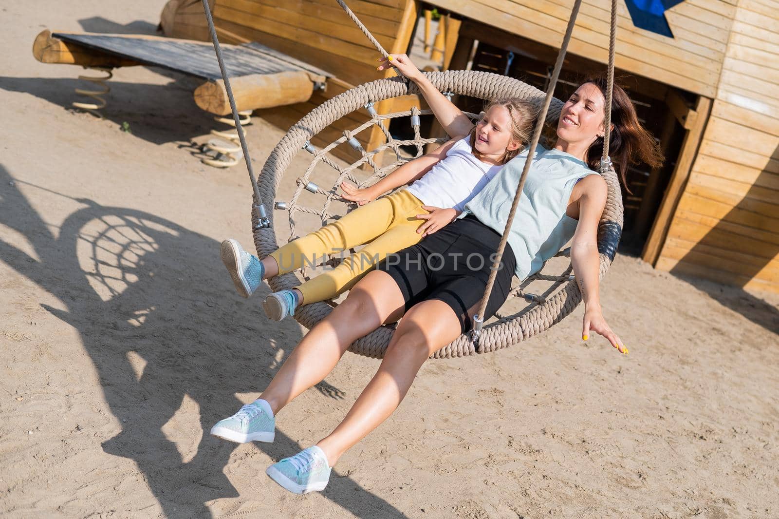 Mom and daughter swing on a round swing. Caucasian woman and little girl have fun on the playground. by mrwed54