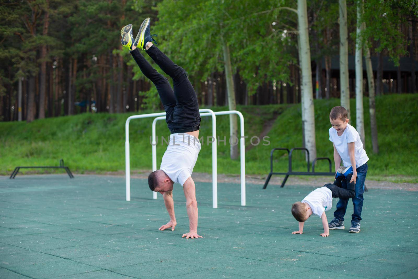 Caucasian man teaching sons handstand at playground outdoors. by mrwed54