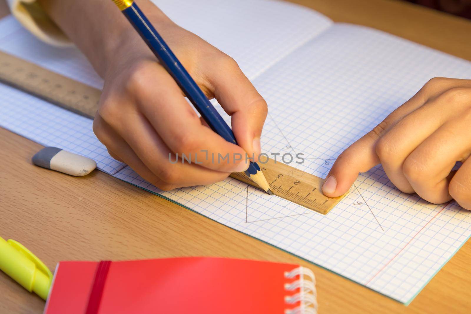 A student draws a line in a notebook with a pencil along a ruler. A schoolboy performs a task at the workplace. The concept of children's education, teaching knowledge, skills and abilities.