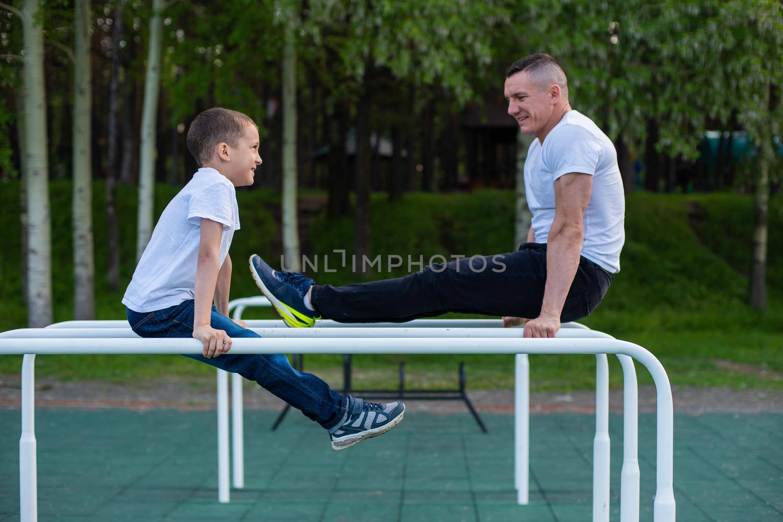 Caucasian man trains a boy on the uneven bars on the playground. Dad and son go in for outdoor sports