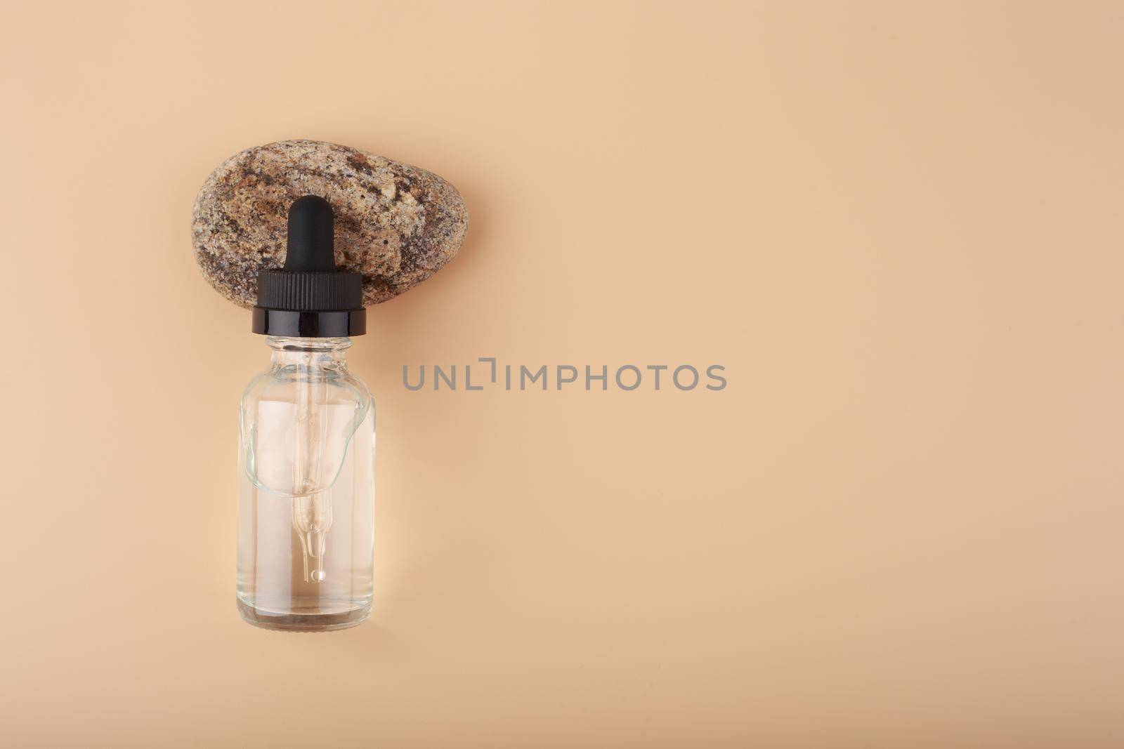 Glass bottle with skin serum or oil for skin care on stone against beige background with copy space by Senorina_Irina