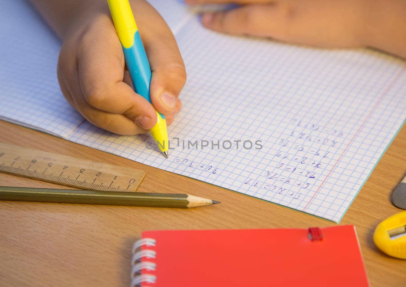 Pupil's hand close-up solves math examples with a ballpoint pen. A schoolboy performs a task at the workplace. The concept of children's education, teaching knowledge, skills and abilities.