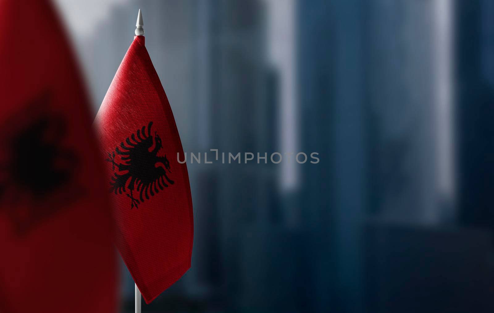 Small flags of Albania on a blurry background of the city.