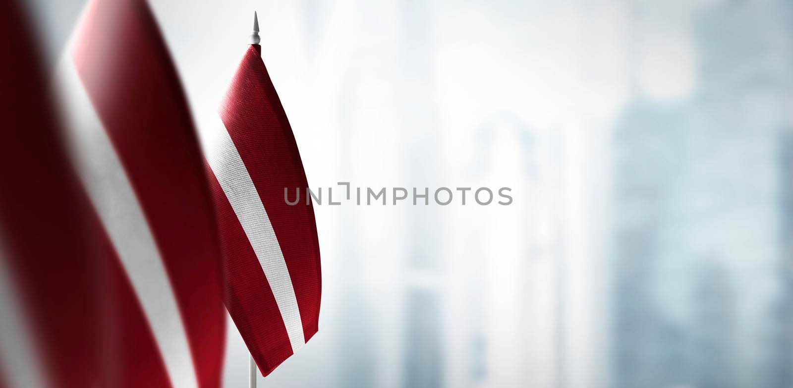 Small flags of Latvia on a blurry background of the city.