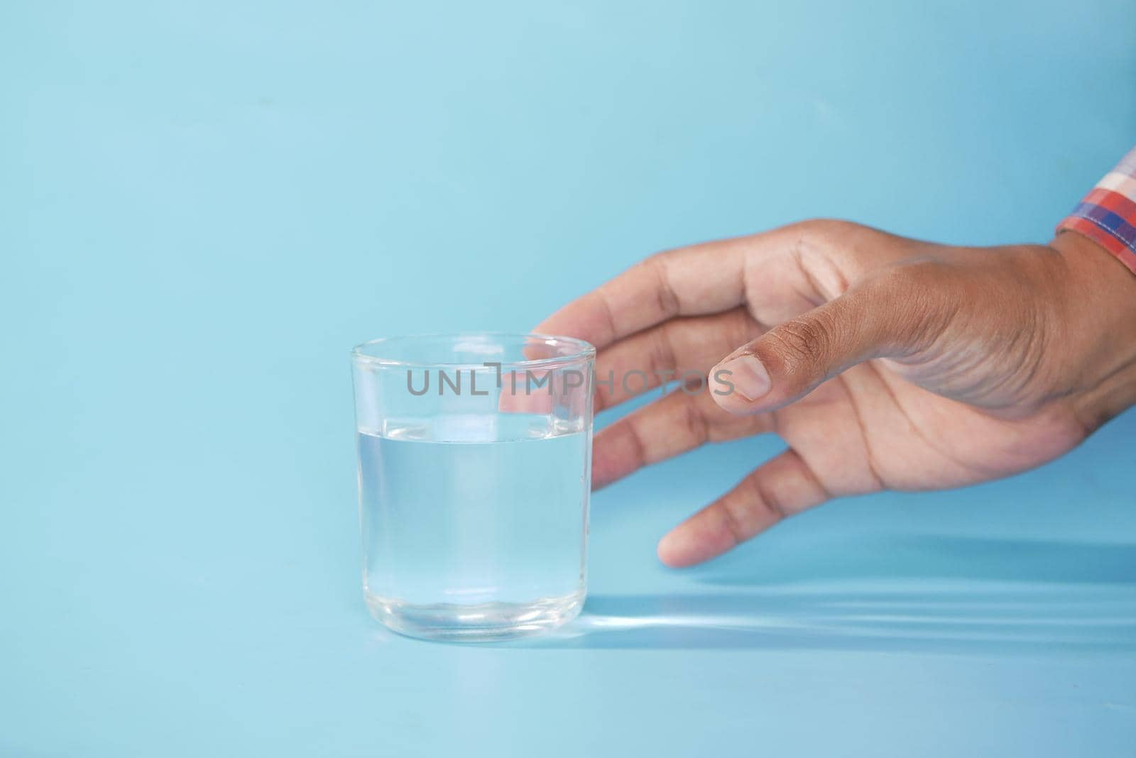 hand holding a glass of water against blue background by towfiq007