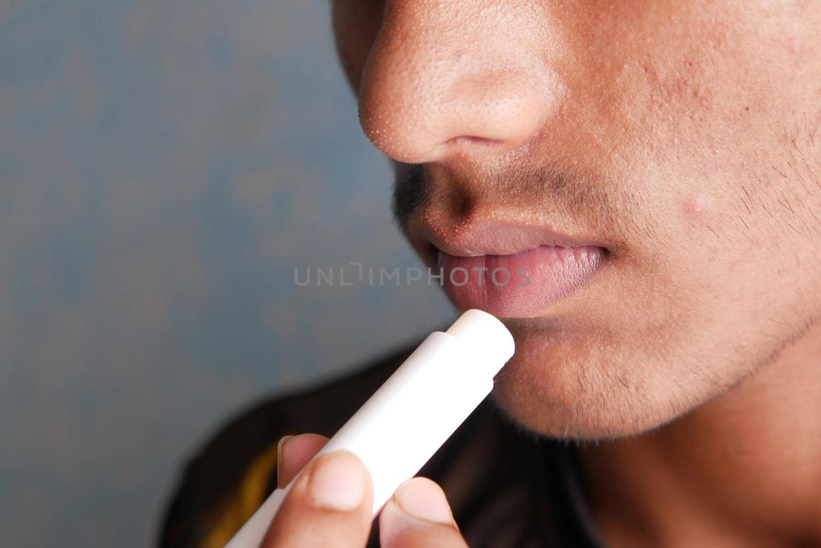 young man applying moisturising lip balm on lips.