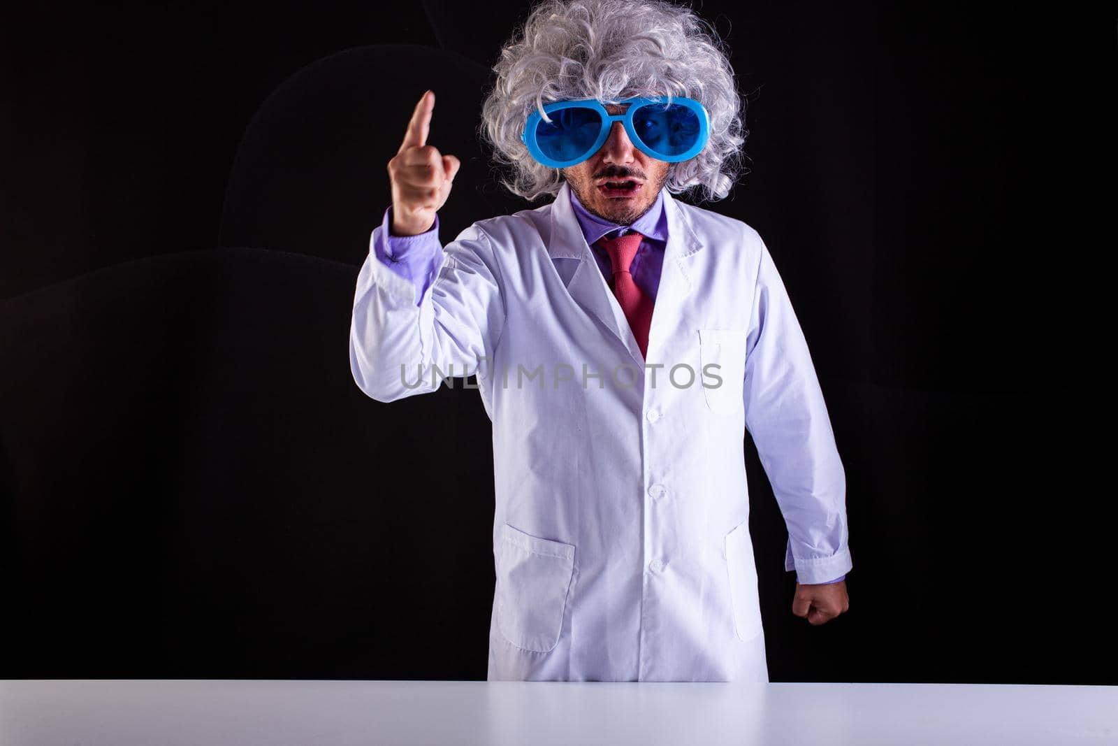 Angry science teacher in white coat with unkempt hair in funny eye glasses with the raised finger