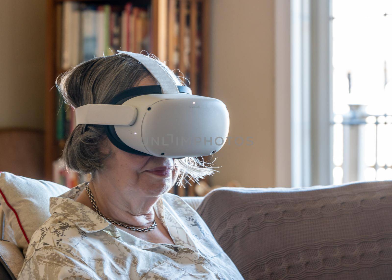 Senior lady seated at home and watching a movie or a quest app on a modern virtual reality VR headset