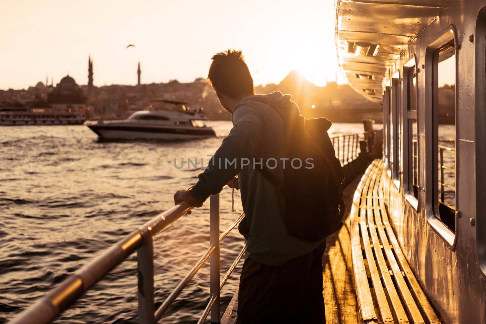 A young travelling man on a ferry floats to the shores of Istanbul, Turkey in the rays of sunset. The beginning of a great adventure.