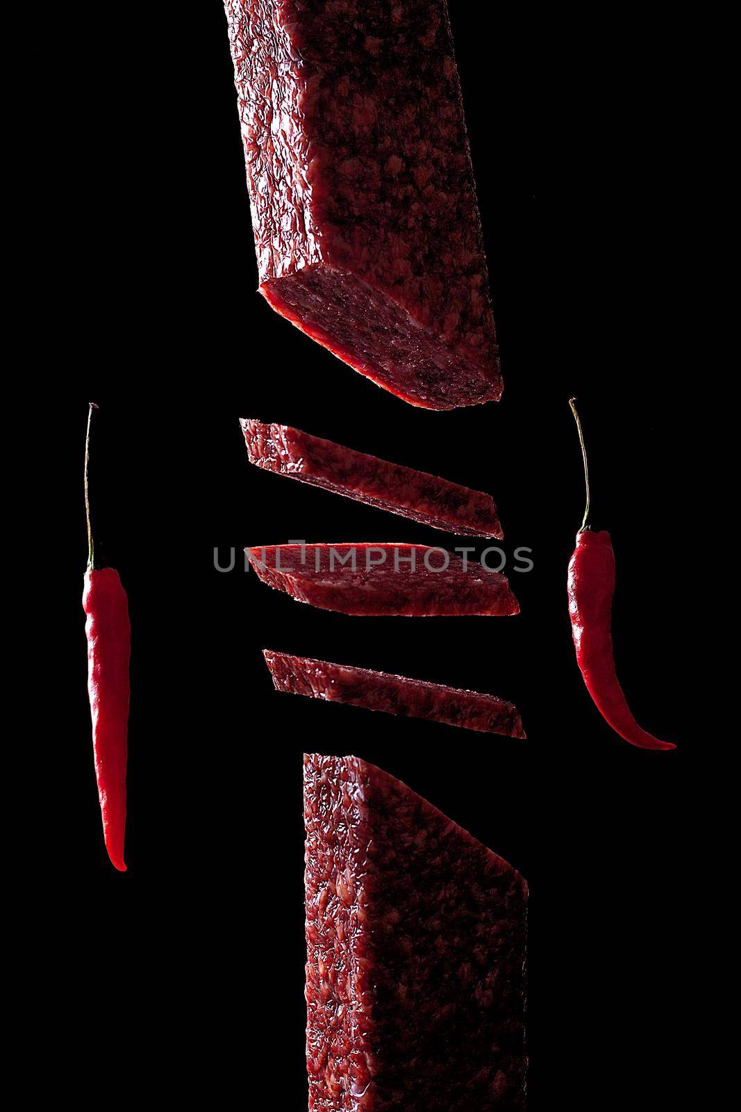 Slice of salami on black background. Flying salami and red pepper.