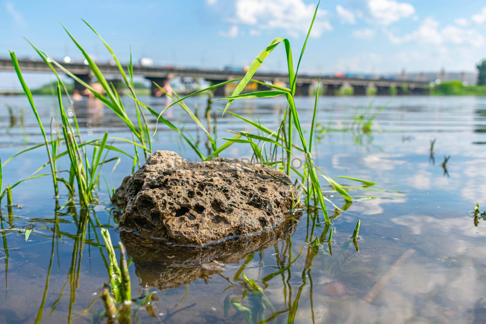 Lonely weathered stone lying in the river against the background of the bridge