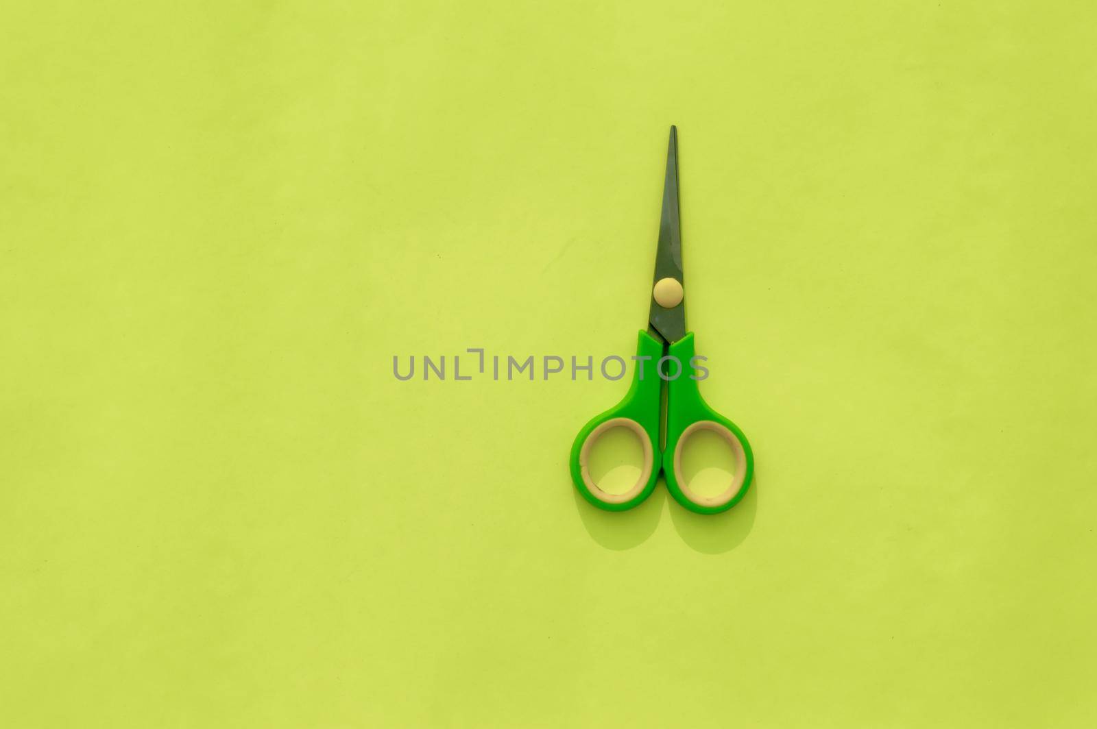 Green scissors isolated on Light green background. Table top view. Copy space for text.