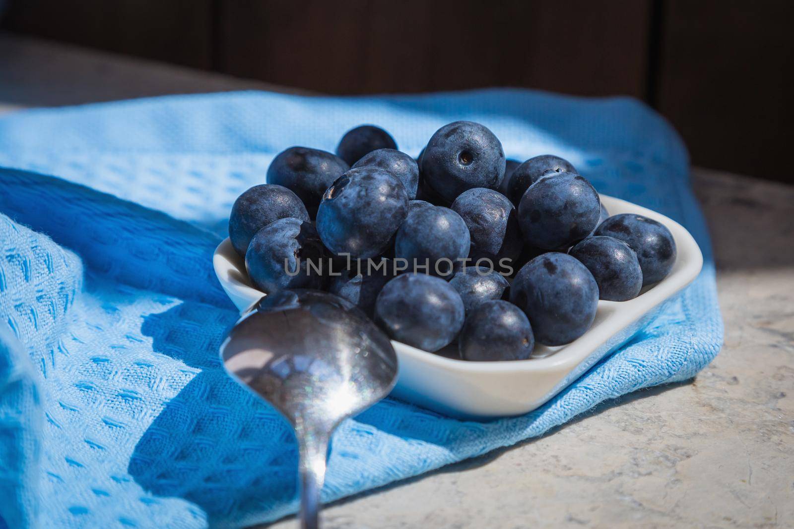 Morning fresh breakfast with fresh blueberries. Blueberries in a white saucer on a blue background. by Yurich32