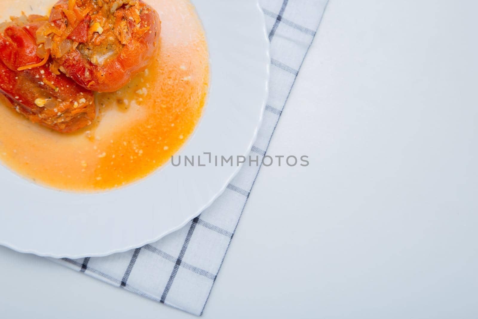 Red pepper stuffed with minced meat and carrots with onions lies on a white plate, which stands on a waffle napkin on a white background. High quality photo