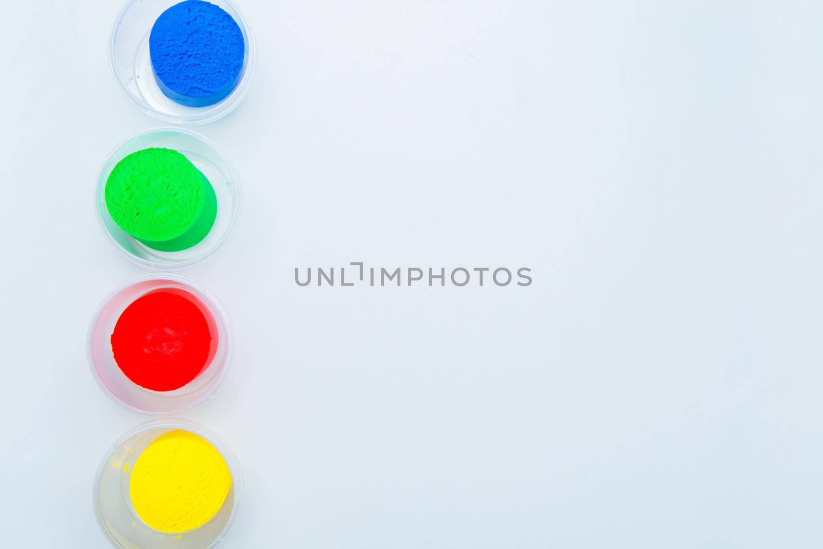 The dough for modeling red, yellow, blue and green colors is placed in a row vertically in jars on the side on a white background. High quality photo