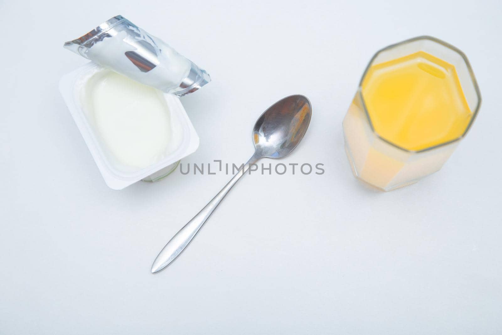 A cup of natural yogurt, a dessert spoon and a glass of orange juice on a white background. High quality photo