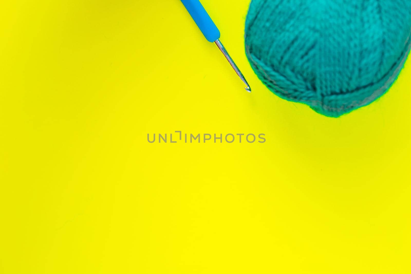 A metal hook with a blue handle lies next to a skein of green yarn in the upper corner of the photo on a yellow background. top view, flat lay, copy space, isolate. High quality photo