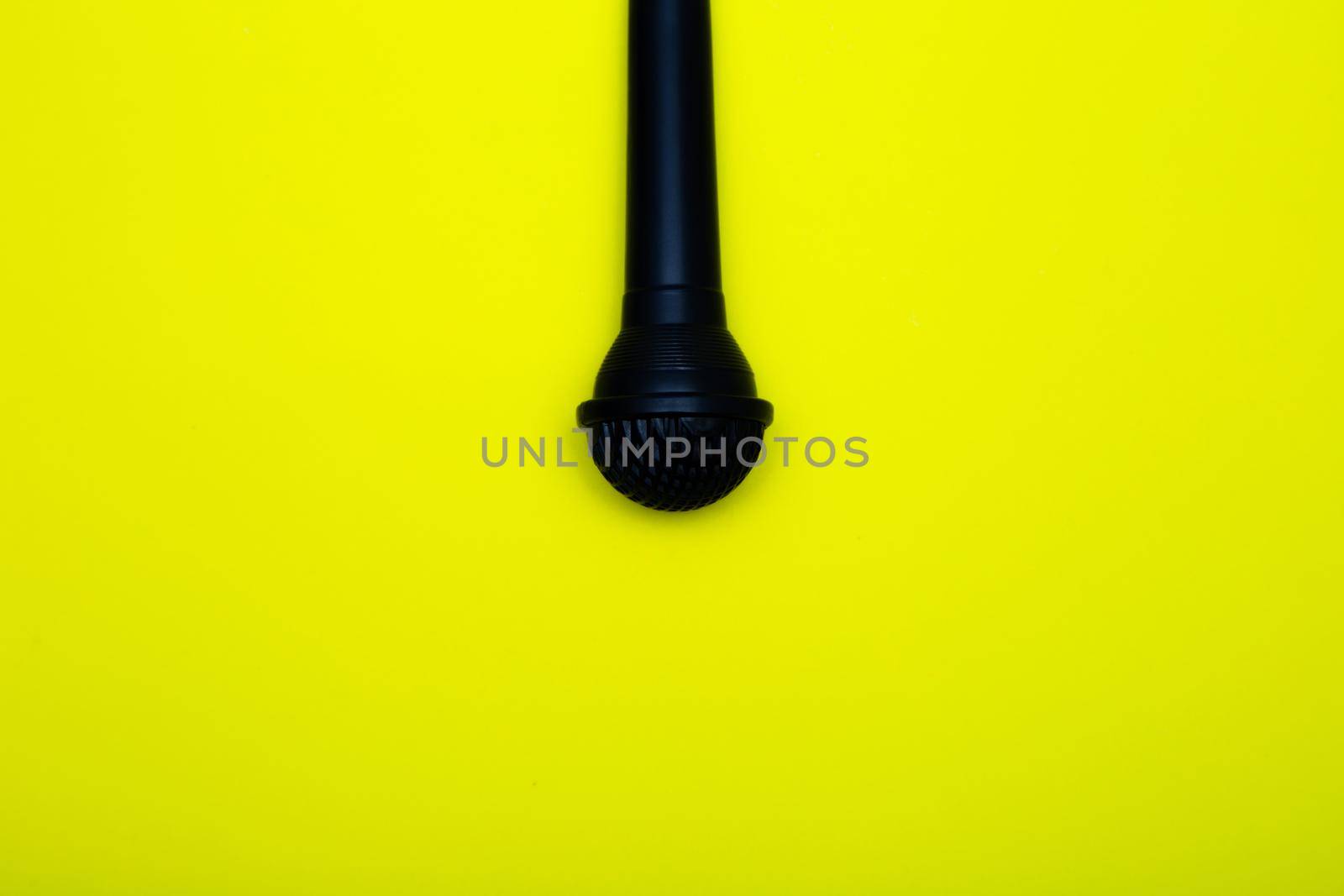 A black microphone hangs from above on a yellow background. High quality photo