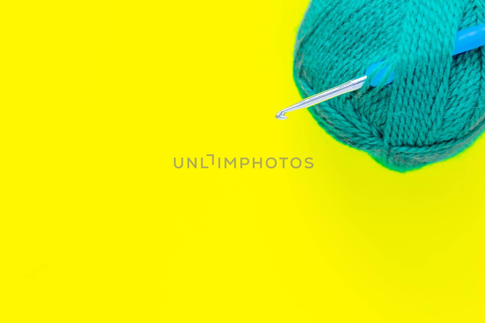 A metal hook with a blue handle is inserted into a skein of green yarn in the upper corner of the photo on a yellow background. top view, flat lay, copy space, isolate. High quality photo