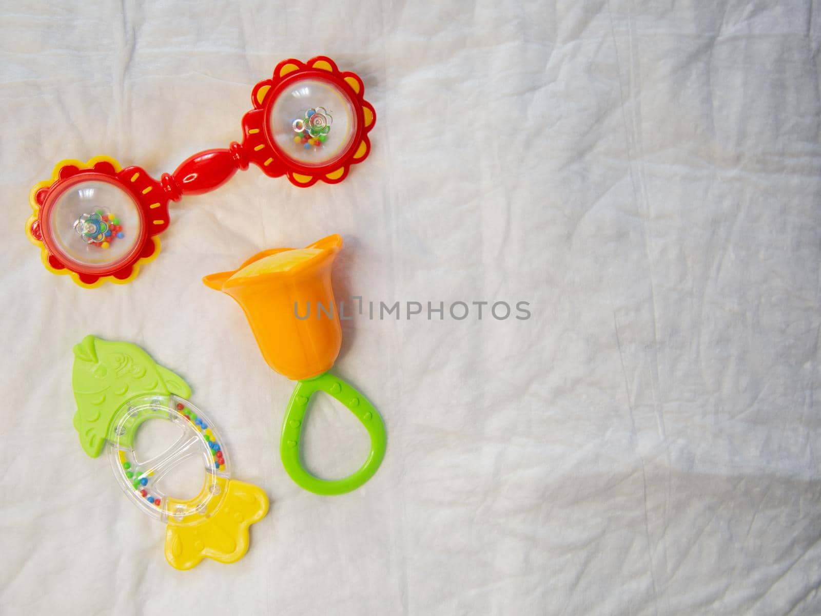 On a crumpled white background there are 3 rattles for newborns. by Kseniia12393