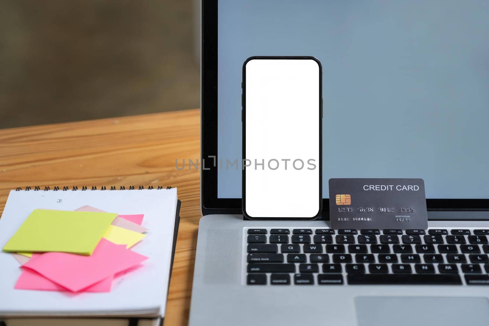 Mock up smartphone device with blank screen standing on laptop computer with credit card. Online shopping concept.